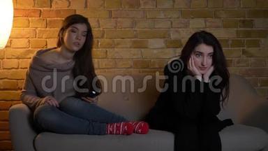 年轻的白种人女孩坐在沙发上，在舒适的家庭背景下<strong>专心</strong>看电视的特写肖像。